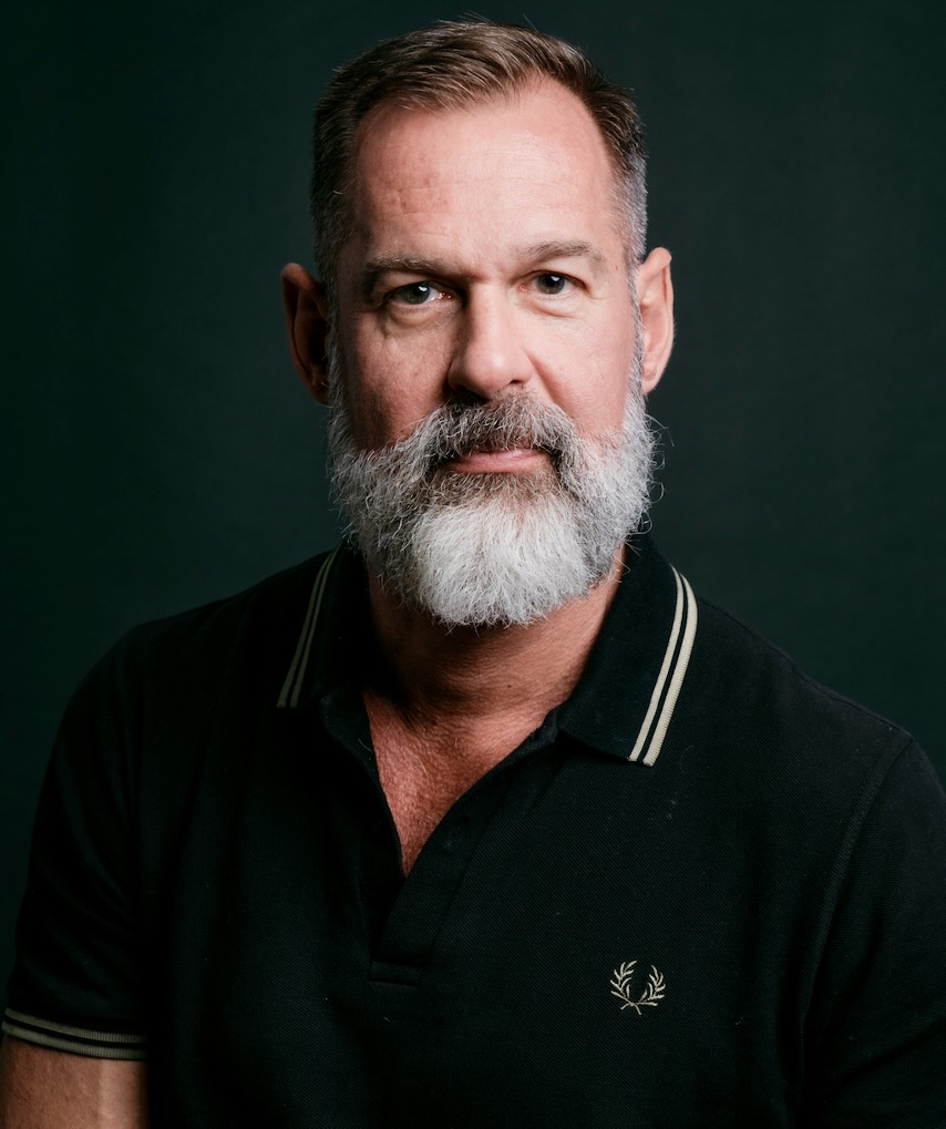 Portrait of Alex Sloan in a black polo shirt against a dark background